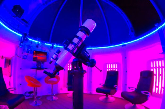 Inside the Airbnb's observatory, complete with a telescope, surrounded by several empty chairs, at night.