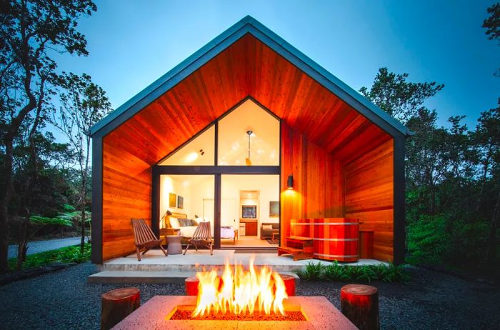 Illuminated firepit in front of the patio of a modern cabin at dusk.