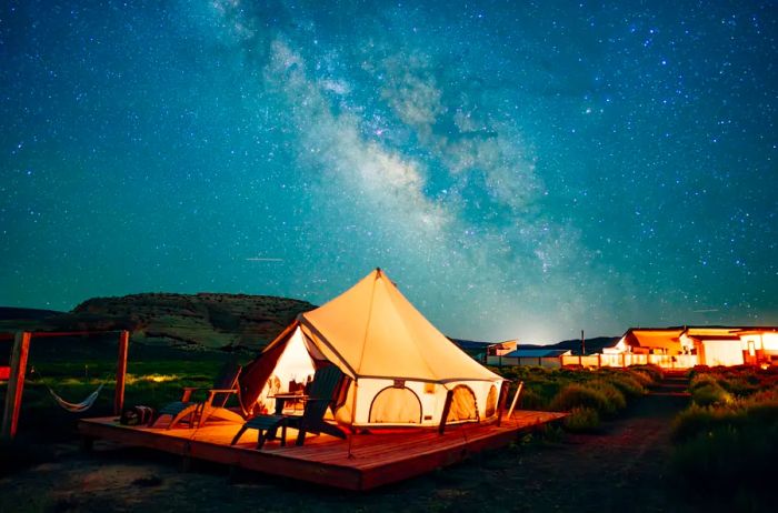 Beige and white bell tent with the Milky Way shimmering overhead at night.