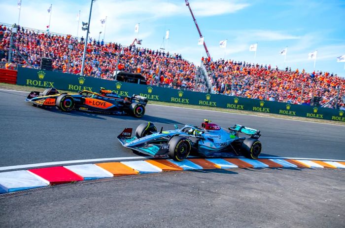 Two race cars competing at the 2022 Dutch Grand Prix F1 championship, with an audience in the background