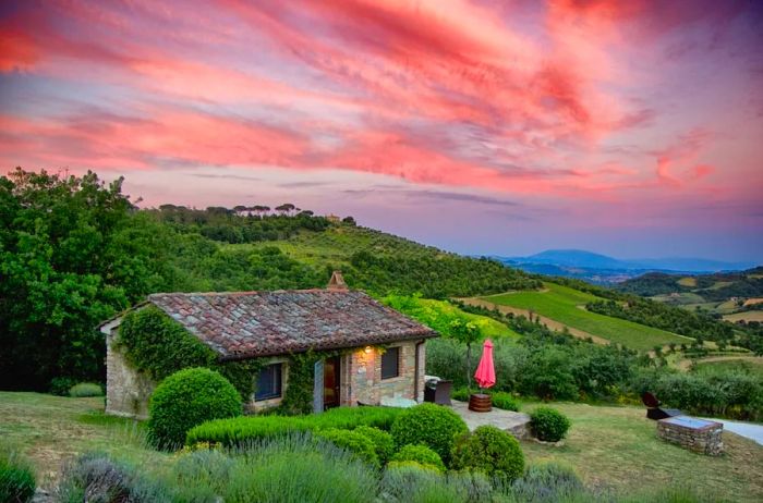 A historic tile-roofed home set against rolling green hills and a sky filled with pink clouds