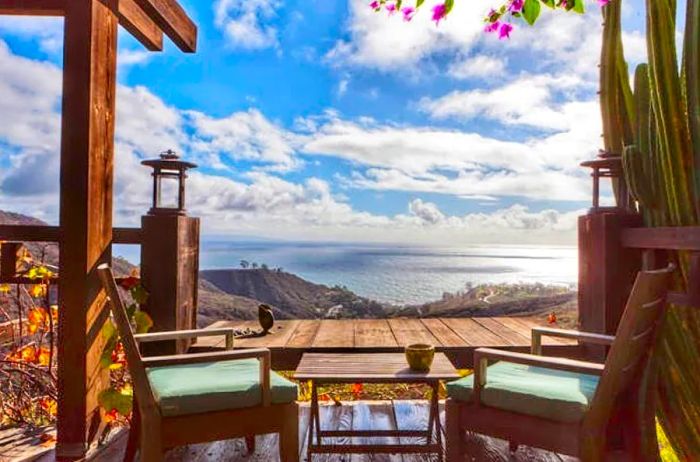 An outdoor seating area adorned with flowers and cacti, overlooking the mountains and the Pacific Ocean