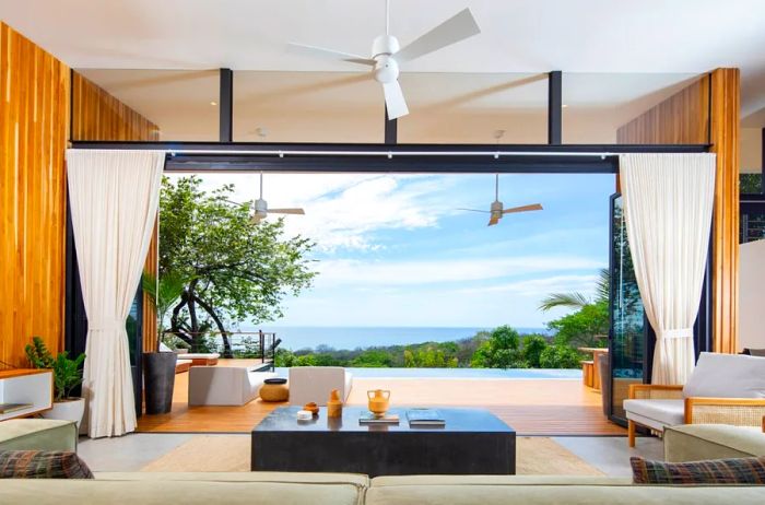 A stylish home with sliding doors that open to views of a jungle and the ocean beyond