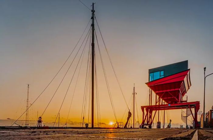 A modern industrial house in red and black overlooking a harbor filled with boats