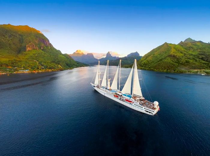 A Windstar sailing vessel navigating the stunning waters of Moorea, set between two lush, hilly islands.