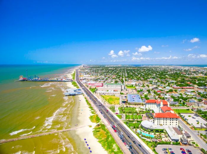 Aerial view showcasing a long beach and city, separated by a roadway