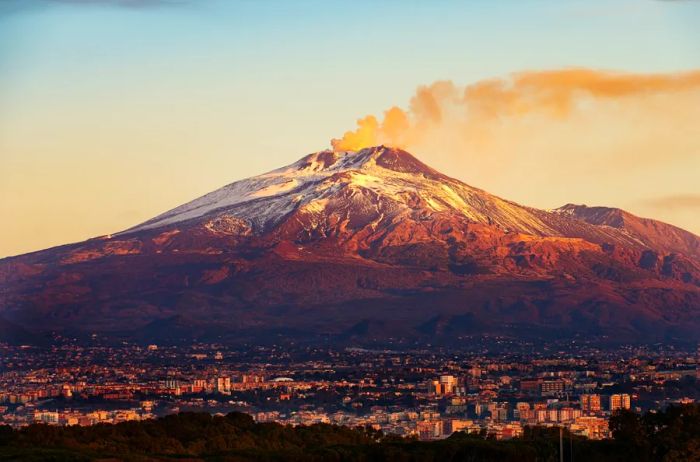 Mount Etna, with its smoky plume, looms over the city of Catania on the island of Sicily, Italy (Sicilia, Italia) spreading out beneath it.