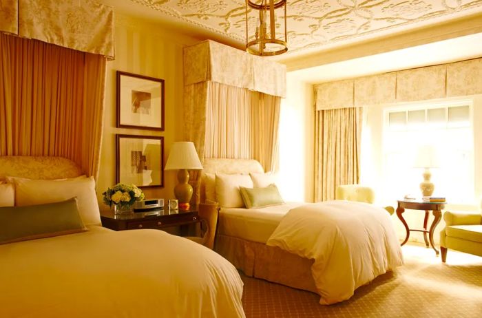 A beige guest room at the Hay-Adams features wingback chairs, canopy beds, a bas-relief ceiling, and floor-to-ceiling curtains at the window.