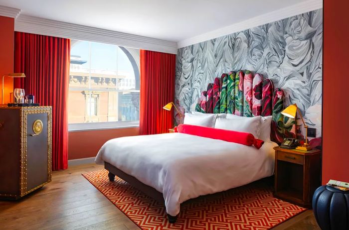 A guest room featuring hardwood floors, a bed topped with a white duvet, marble-patterned wallpaper, and rusty orange drapes.