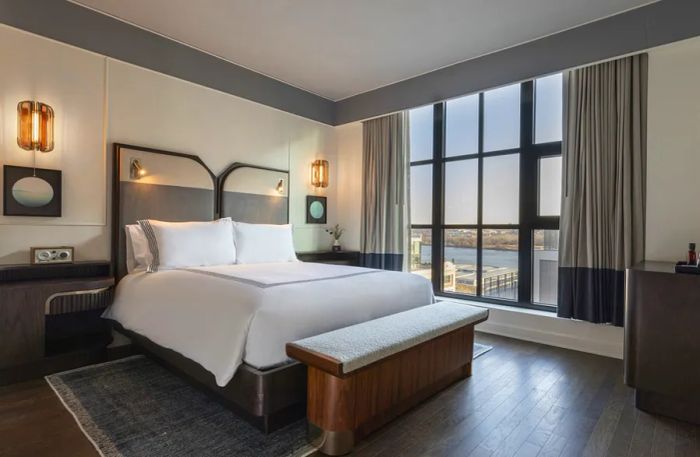 A spacious guest room at Thompson Washington, D.C., featuring hardwood floors and large windows adorned with gray drapes.