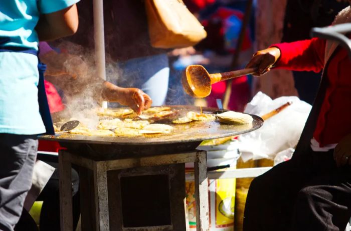 A Mexican street vendor preparing fry tacos filled with meat and drizzled with sauce.