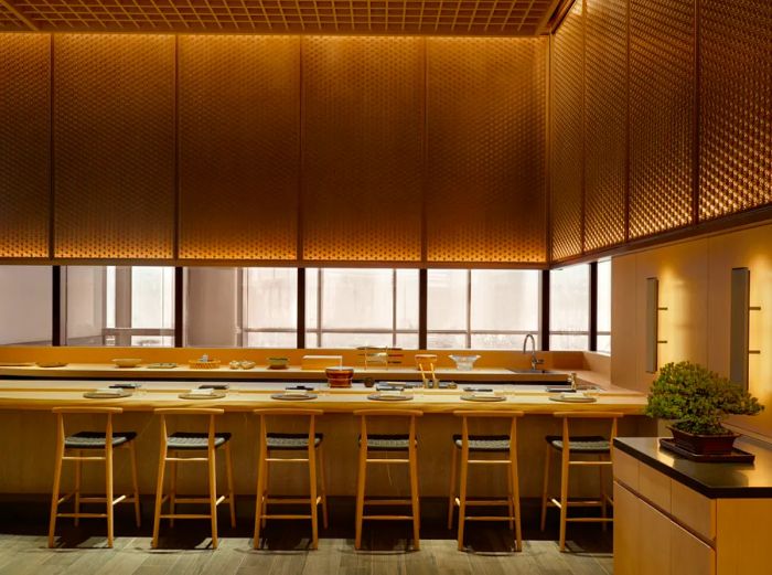 Iigura sushi restaurant features a long hinoki wood counter with six tall chairs and place settings, complemented by a bonsai tree on the right.