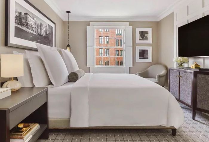 A light gray guest room at the Rosewood Washington D.C., featuring large black-and-white photographs, a carpeted floor, and a large flat-screen TV.