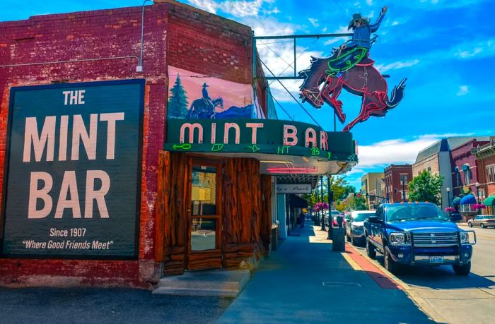 The brick and wooden exterior of Mint Bar, the oldest bar in Sheridan, features a neon sign of a cowboy riding a bucking horse.