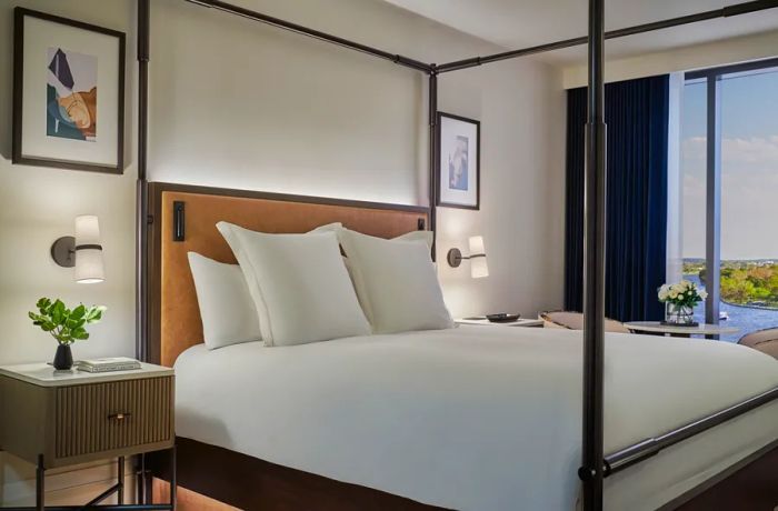 A bright guest room at Pendry Washington D.C. features a four-poster bed and framed artwork.