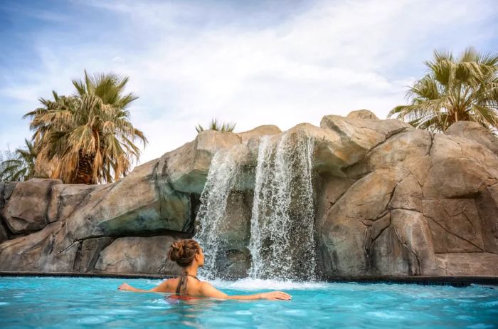 A woman enjoys a poolside retreat surrounded by rocks and a waterfall at The Spa at Séc-he in Palm Springs.