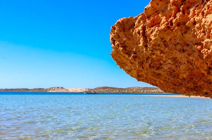 The blue, shallow waters of the Ningaloo Coast, featuring a porous overhanging rock on the right