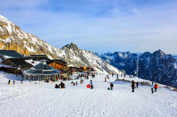 People gathered near a snow-covered mountain hut surrounded by woods.