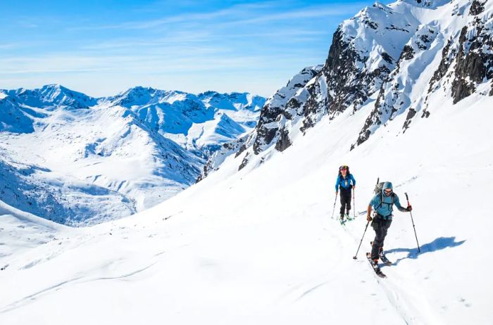 Two skiers ascend the slopes on a warm, sunny day in the backcountry of Alaska's Talkeetna Mountains.