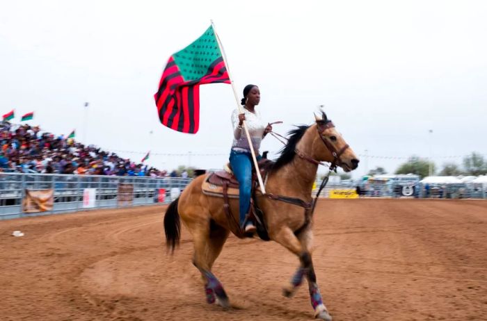 Rider holding a flag on horseback at a Black Rodeo