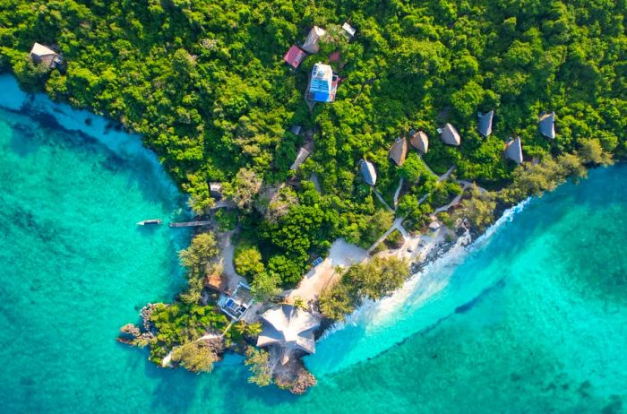 An aerial view of Chumbe Island Resort reveals its stunning blue waters contrasted with lush green forests.