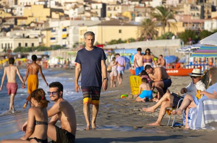 Dominic (Michael Imperioli) strolls along Cefalù Beach, a filming site for 