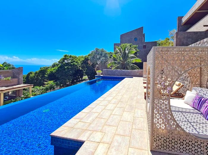 The exterior of a hillside suite at Coulibri Ridge features an infinity pool under a clear blue sky.