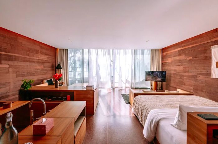 The interior of a guest room at Potato Head Studios in Bali, Indonesia, showcases dark wooden walls, a cream-colored blanket, and a television.