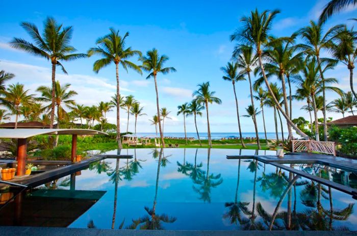 A resort pool at Four Seasons Hualalai, mirroring the lush palm trees surrounding it.