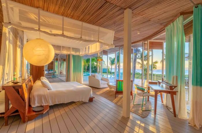 The ocean-view master bedroom of a private villa at Miavana on Nosy Ankao, Madagascar, features a canopied bed, blue and white drapes, and several lounging chairs.