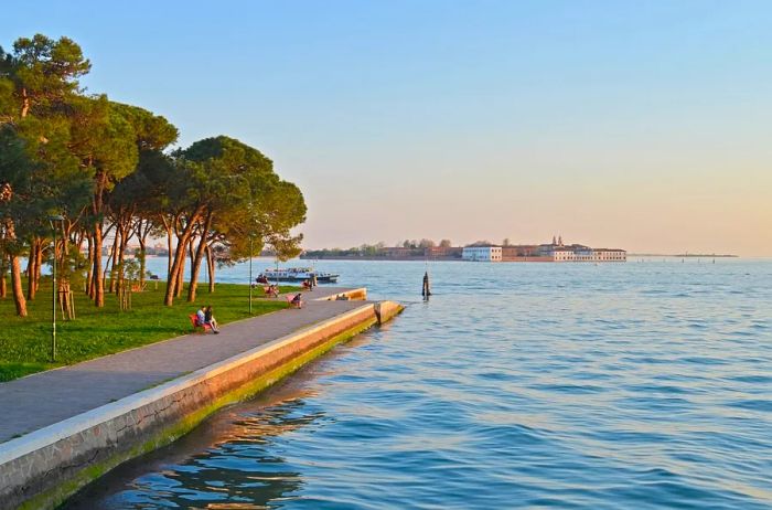 A picturesque walkway next to the water at Venice’s Parco delle Rimembranze, framed by lush greenery on the left.