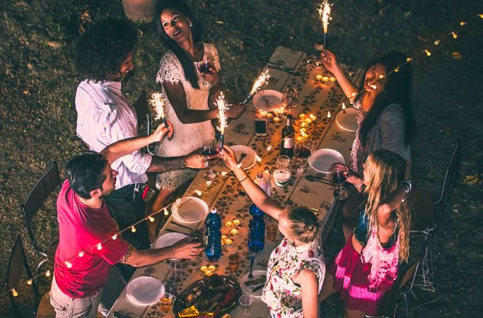 Aerial view of friends outside, toasting over a beautifully set table adorned with string lights.