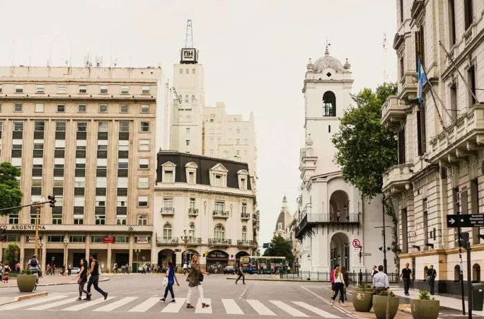 People walking across a street in Buenos Aires, Argentina, surrounded by an array of historic gray, white, and cream buildings.