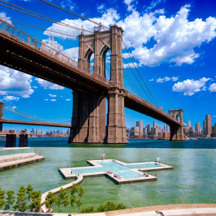 A plus sign-shaped pool in the river beneath the Brooklyn Bridge, framed by the city skyline