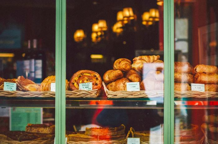 A view of croissants, pain au chocolat, and other delightful French pastries through a shop window