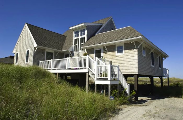 A large light-gray cottage exterior featuring white stairs, surrounded by lush tall grass