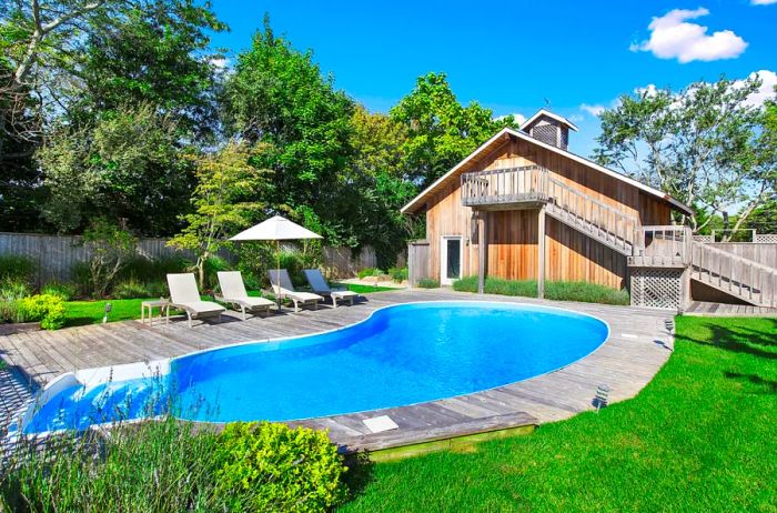 Wooden house set behind a kidney-shaped pool, surrounded by a deck and lush green lawn