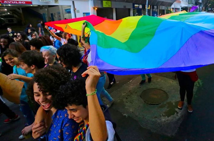 Activists wave a large rainbow flag in a bustling crowd.