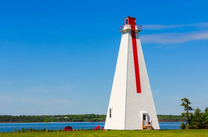 White pyramid-shaped lighthouse with a vertical red stripe on a flat shoreline