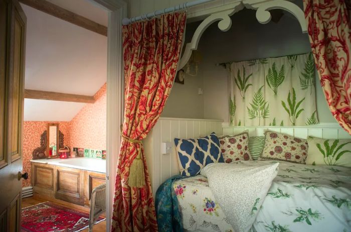 Bed nestled in an alcove, adorned with curtains and floral-patterned linens and pillows, with a bathroom to the left