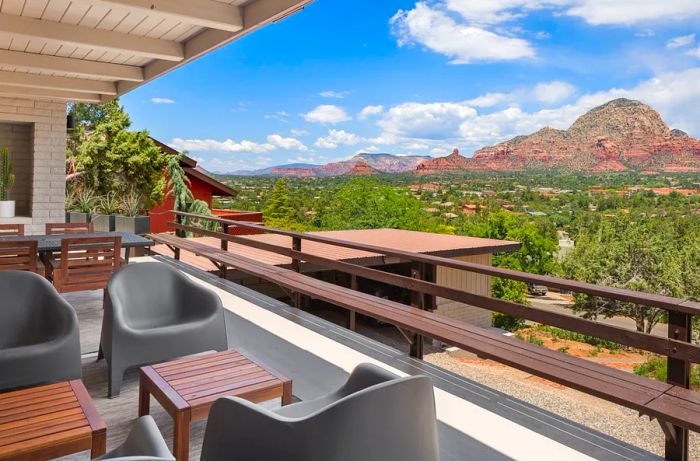 Spacious deck furnished with chairs and small tables, featuring rugged red hills in the background