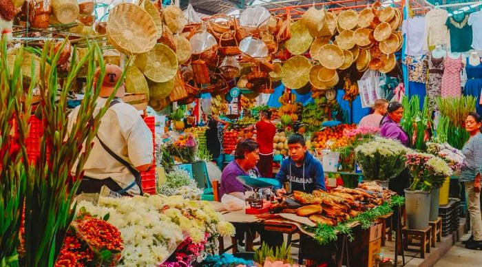 People seated in a bustling food market, with empty baskets hanging above