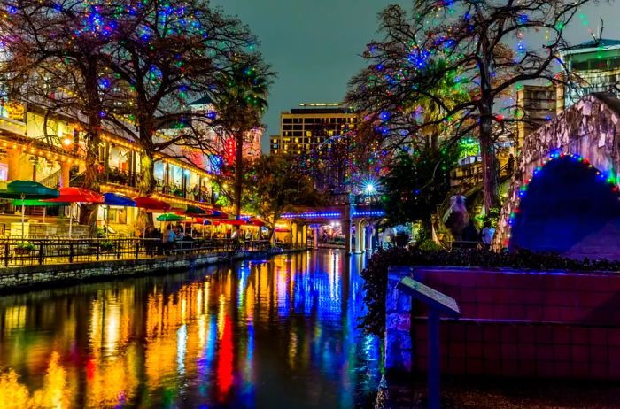 A nighttime view of the historic Texas River Walk adorned with Christmas lights on a rainy evening in San Antonio, Texas.