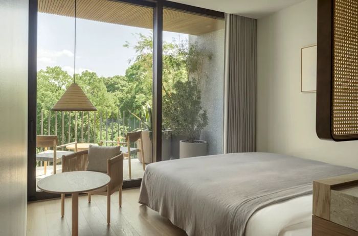 Guest room interior at Trunk(Hotel) Yoyogi Park showcasing natural wood accents and gray tones; a floor-to-ceiling glass wall opens to a deck with views of the adjacent park.