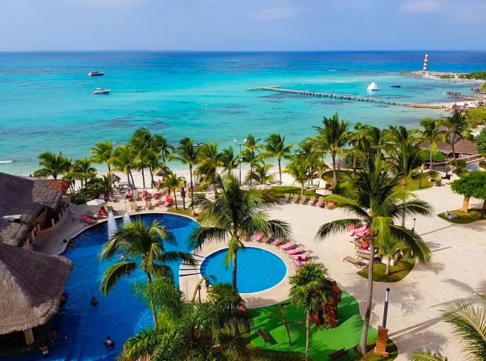 Aerial view of a resort featuring two pools next to the beach, surrounded by palm trees