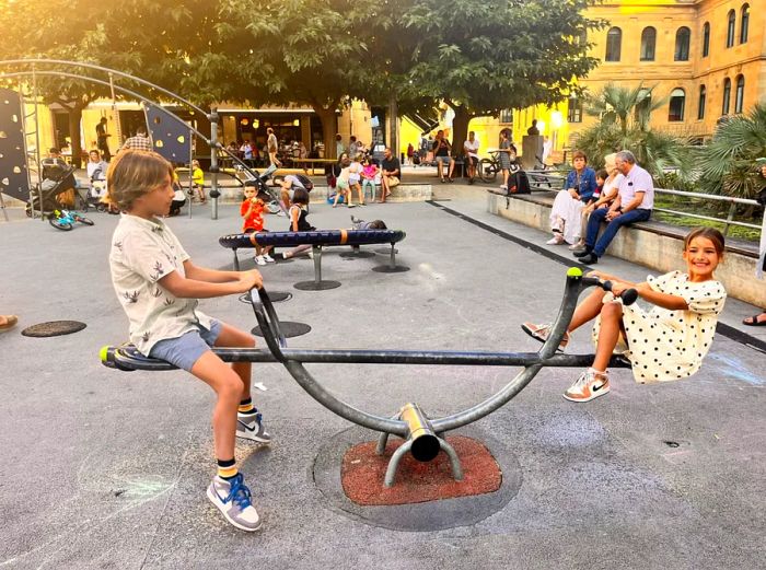 Two children playing on a see-saw in a bustling playground in San Sebastián, Spain