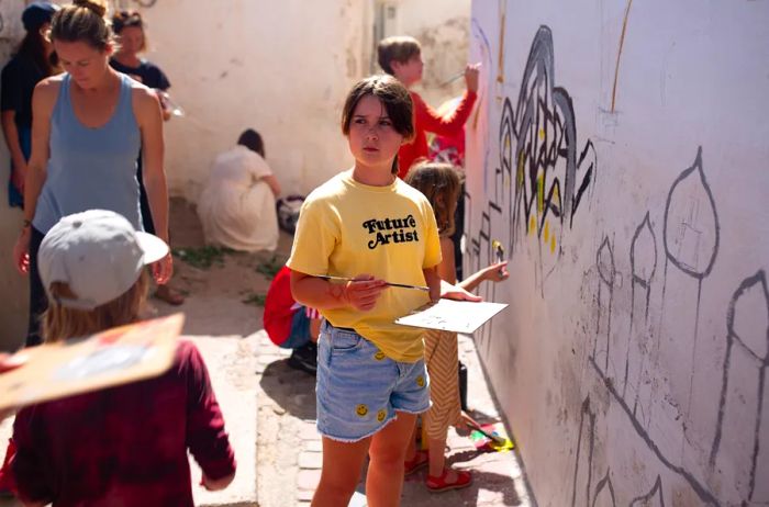 A group of individuals creates a mural in Morocco during a Quartier Collective event, featuring a girl in a yellow T-shirt emblazoned with 