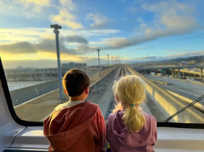 Two small children seated by the large front window of the AirTrain at San Francisco International Airport