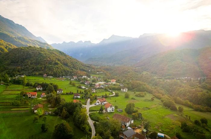 Aerial view of the serene rural landscape of Bosnia and Herzegovina, featuring a winding road and a few scattered homes