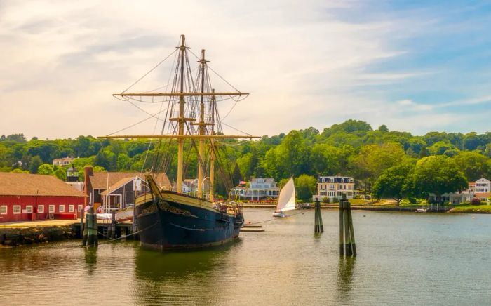 The exterior of Mystic Seaport, a recreated 19th-century village and educational maritime museum, featuring a majestic masted ship.